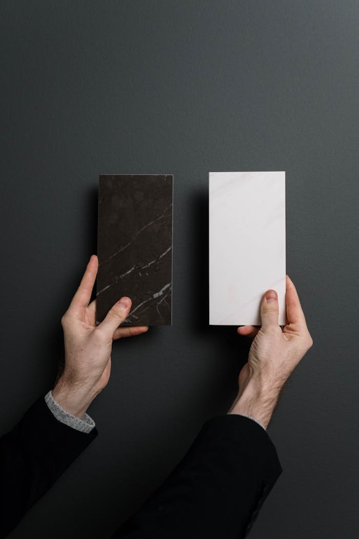 Studio shot of hands holding contrasting marble and stone tiles on a black background.